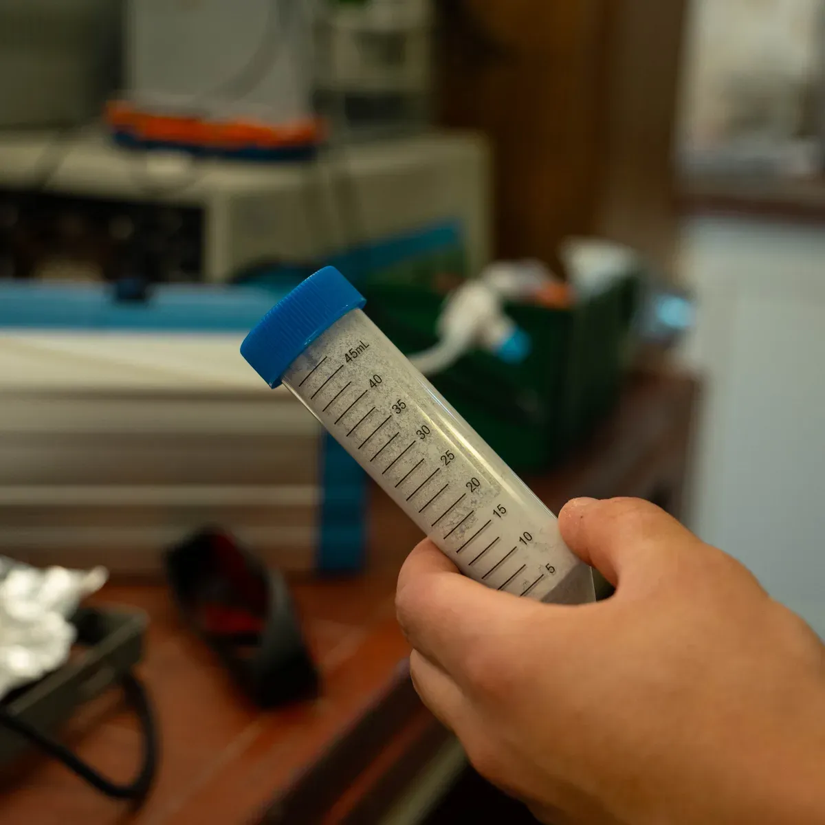 A hand holding a graduated 50 mL centrifuge tube, marked in 5 mL increments up to 45 mL, part filled with a cloudy solution.
